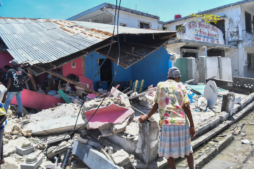 A woman stands in front of a destroyed home in the aftermath of an earthquake in Les Cayes.