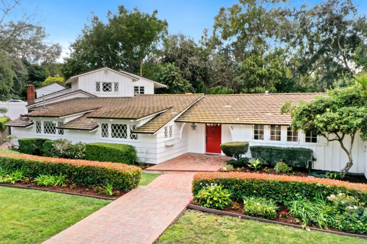 california ranch style home with a red door and pruned landscape